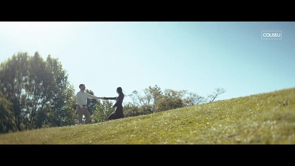 Casal dança em campo aberto numa colina verde, frame do filme da Coliseu