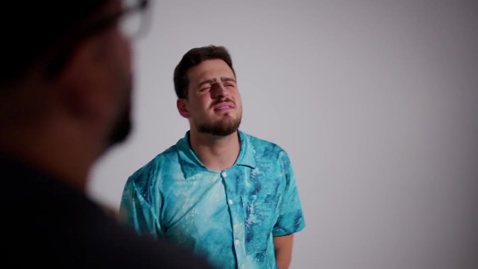 Cantor de camisa estampada se apresenta em estúdio de fundo branco, frame do filme Drinkiss