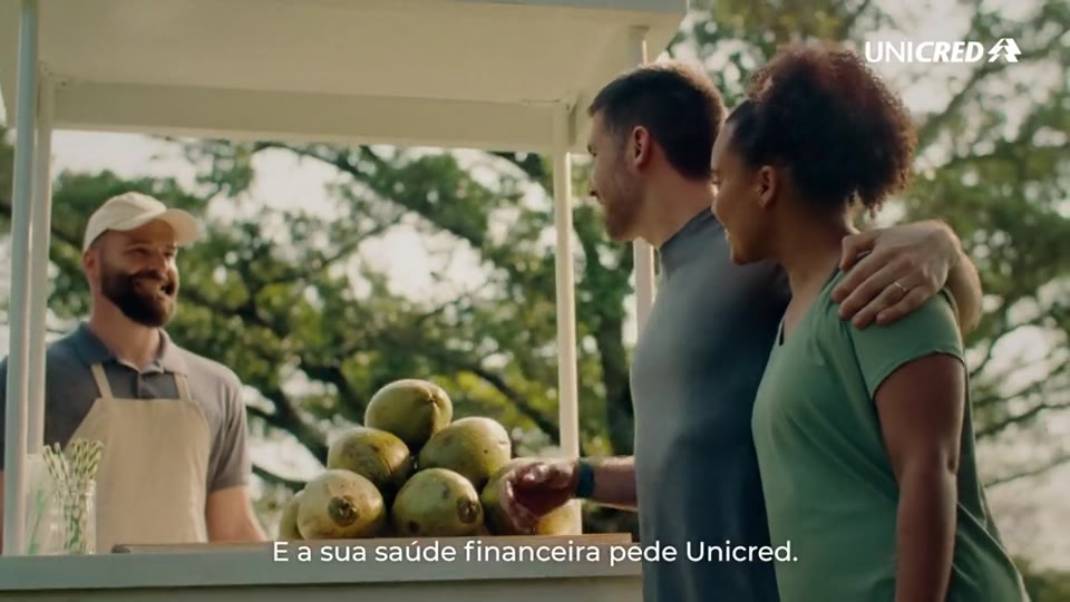 Casal conversa com feirante em banca de frutas ao ar livre, frame do filme da Unicred